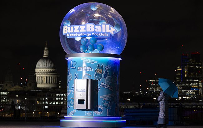 A large scale blue gacha machine, covered in emojis and pictures of labubu-style toys